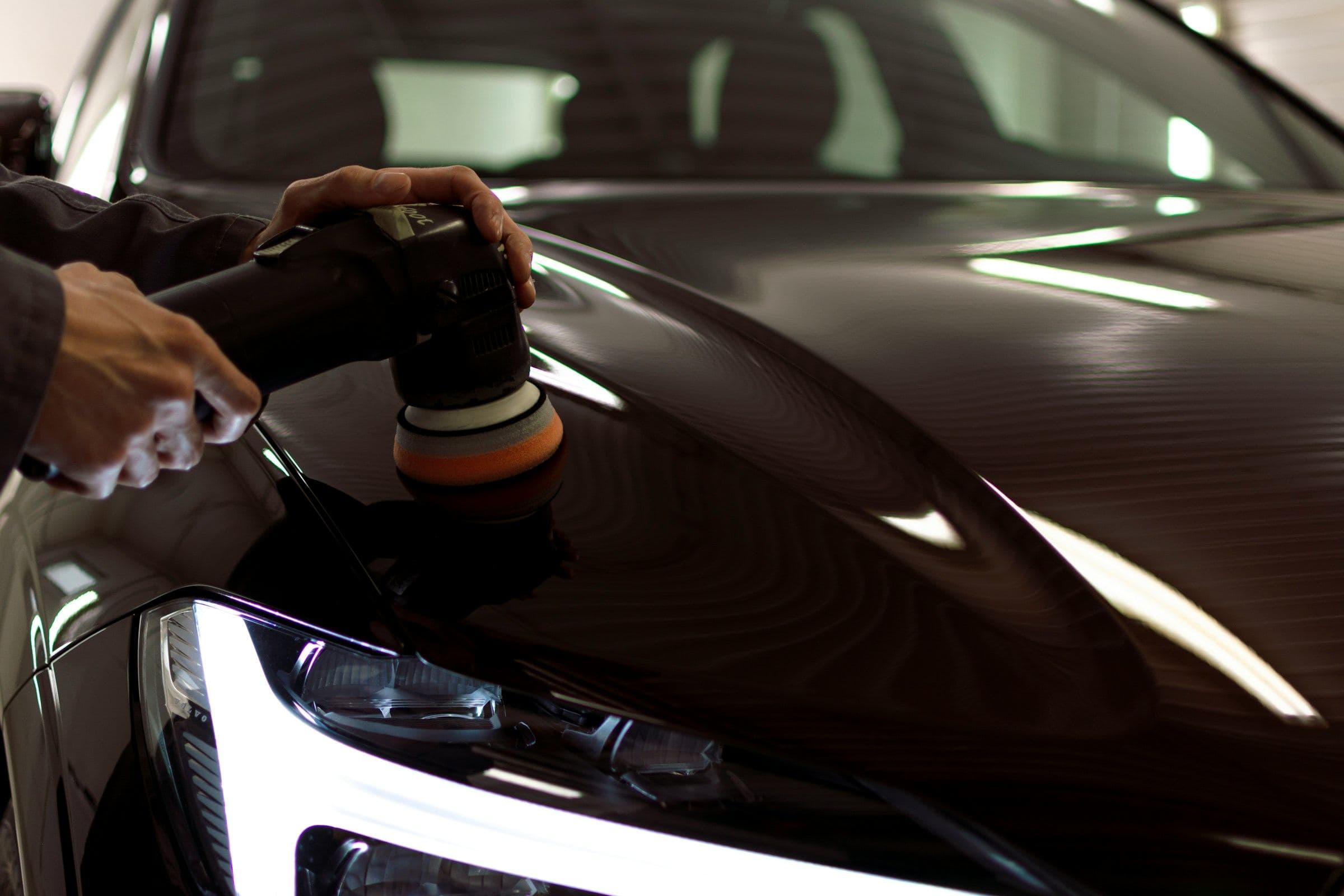 Polisher restoring the finish on a dark car's hood