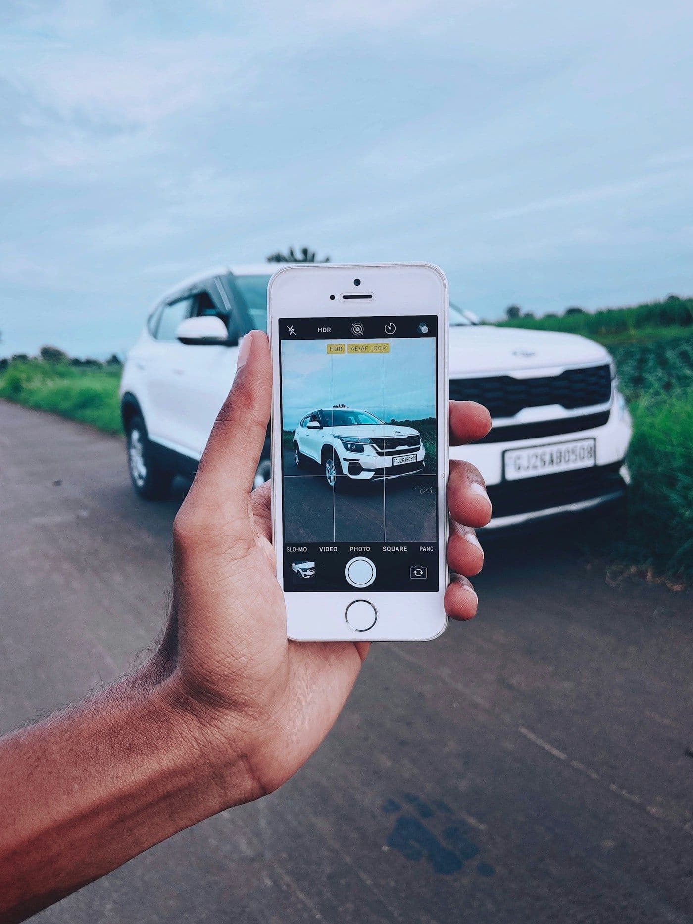 Hand holding a phone, framing a photo of a white SUV