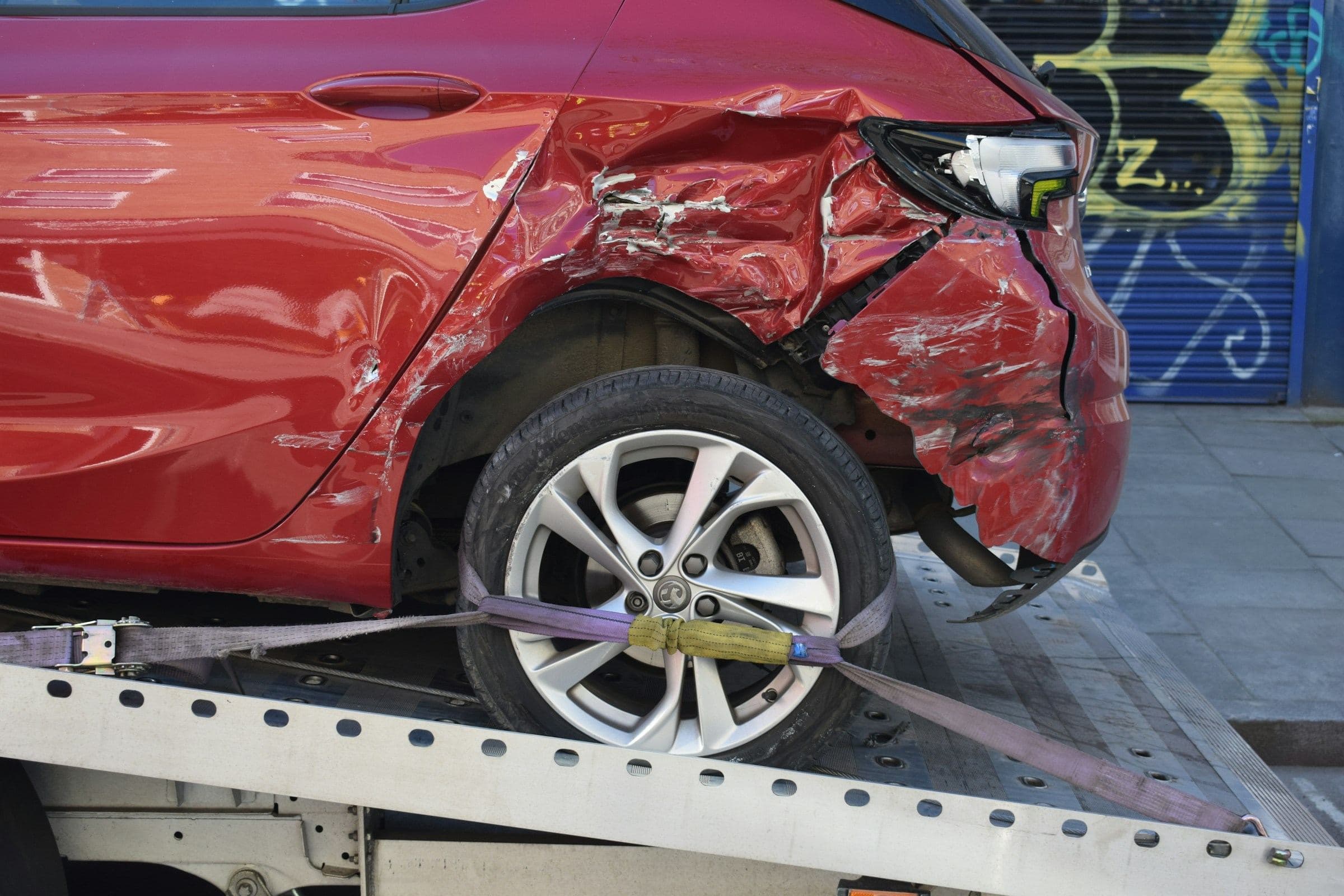 Damaged red car strapped to a flatbed tow truck